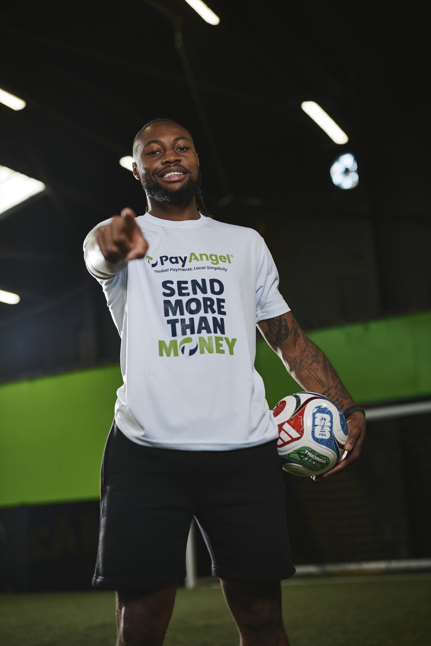 Antoine Semenyo in a PayAngel Send More Than Money shirt, pointing towards the camera and holding a football.